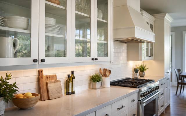A white kitchen with glass-front upper cabinets on each side of the range hood.